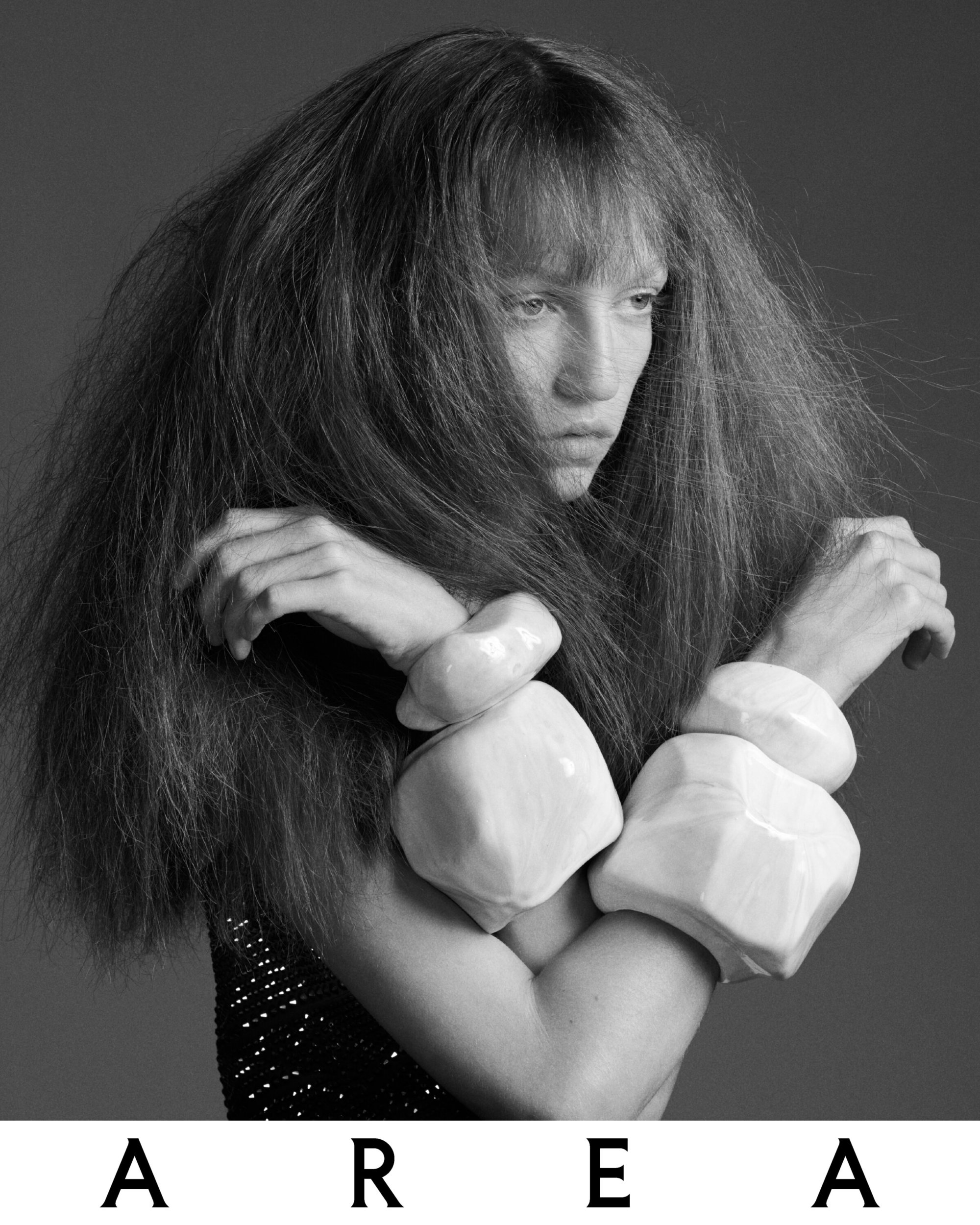 Monochrome portrait of a woman with voluminous textured hair wearing large sculptural bracelets, shot for Area.