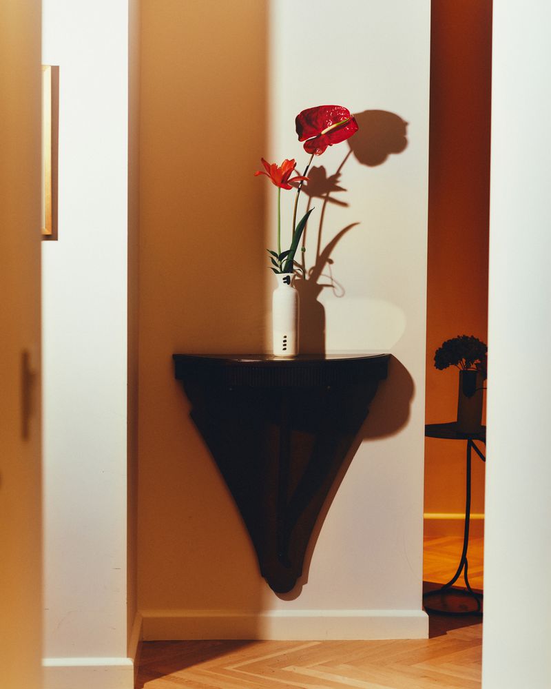Indoor shot showcases a vibrant red anthurium flower arrangement on a dark wood console table against white walls with herringbone wood flooring.