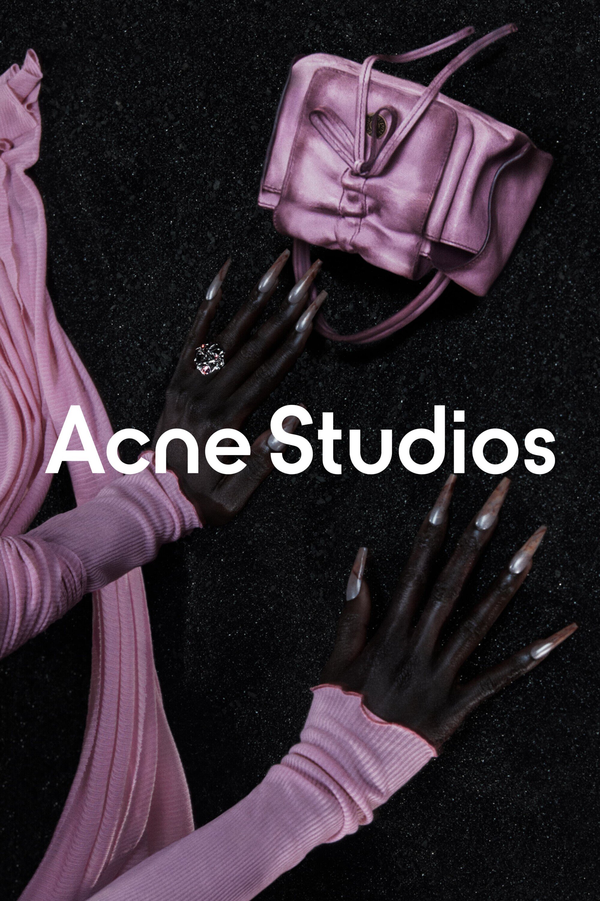 Fashion still life featuring an Acne Studios bag, manicured hands with long nails, a silver ring, and a pink knitted garment on black fabric.