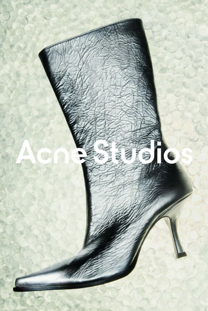 Studio shot of a black leather heeled boot by Acne Studios on a textured white background, showcased for fashion and style.