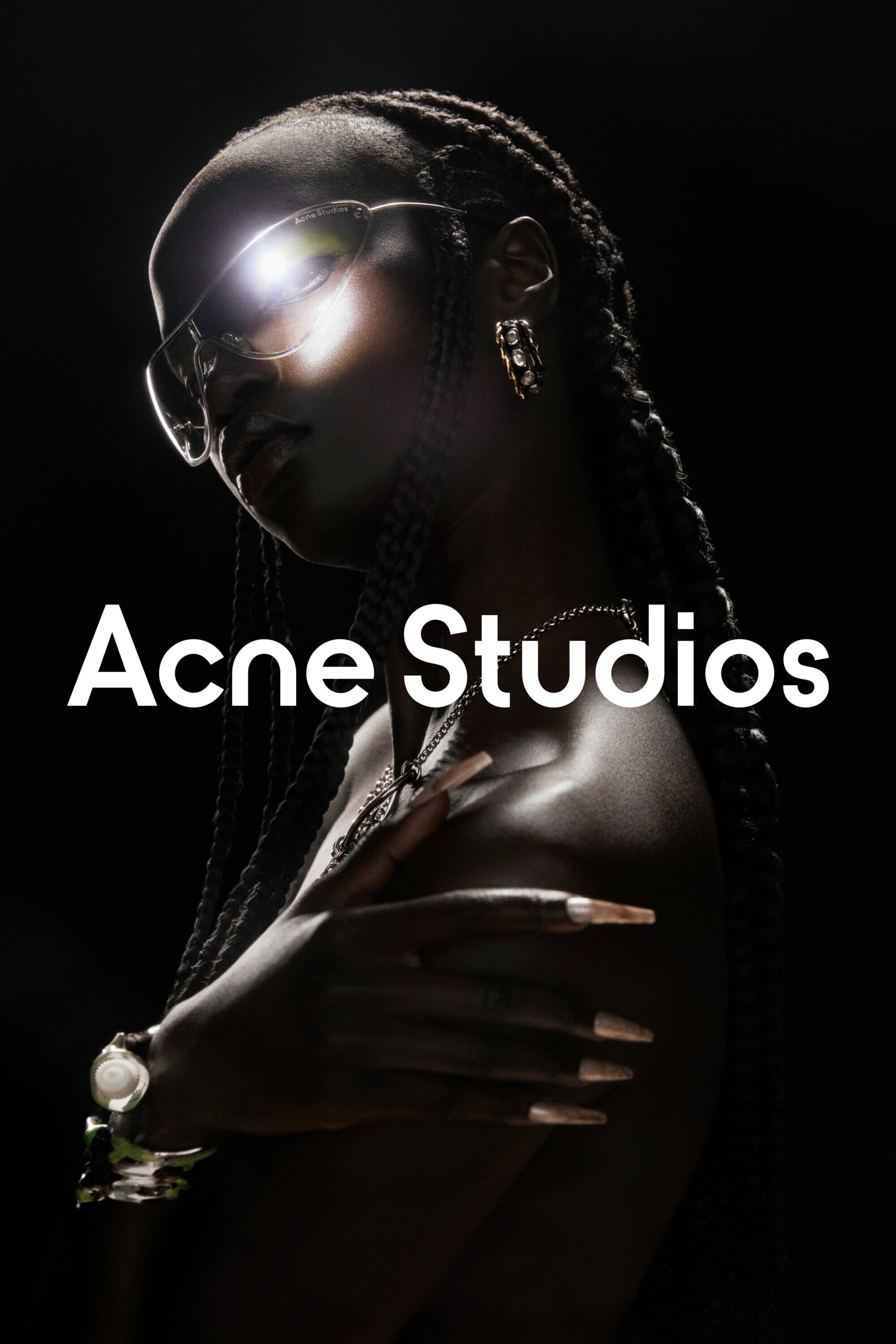 Portrait of a Black woman with glasses and braids, side profile, wearing jewelry, with Acne Studios text overlayed against a dark background.