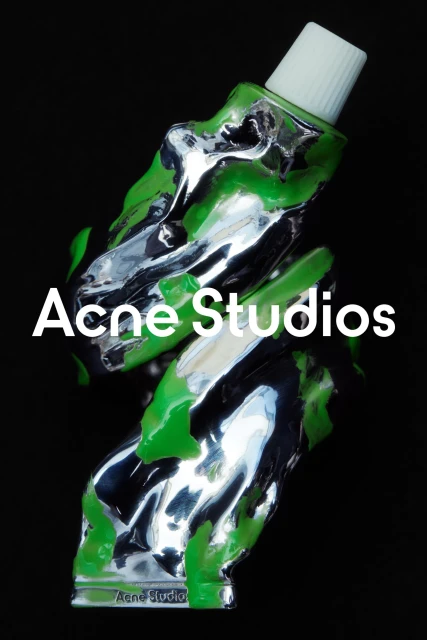 Abstract product shot: a metallic tube with green paint against a dark background features Acne Studios branding for visual interest.