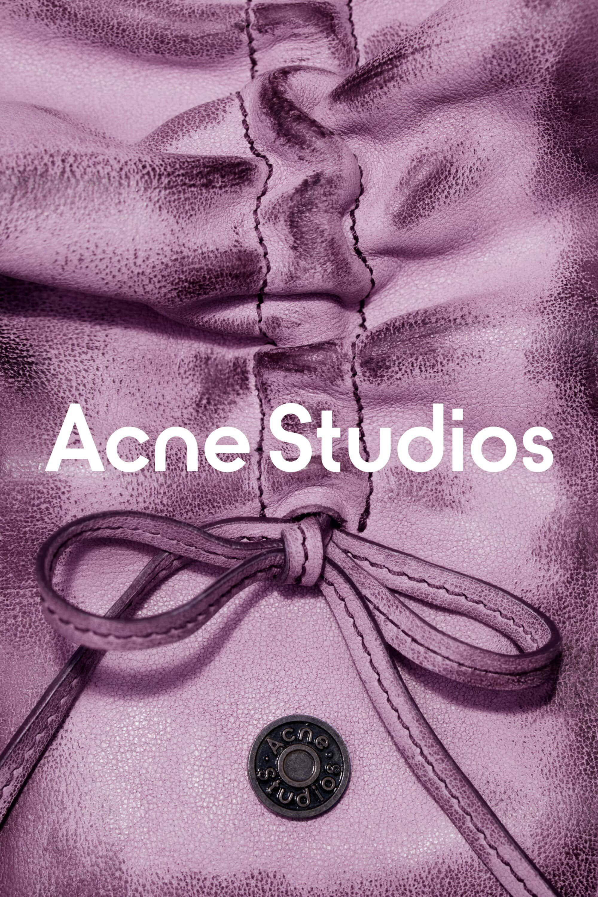 Close-up of a gathered and knotted lilac leather bag with a metal button, featuring the 'Acne Studios' logo in white text.