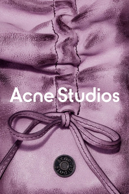 Close-up of a gathered and knotted lilac leather bag with a metal button, featuring the 'Acne Studios' logo in white text.