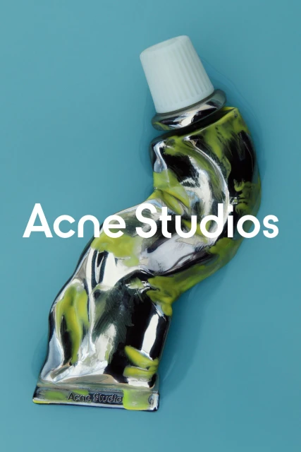 Still life featuring a shiny, manipulated tube of paint in silver and green with white cap set against a solid light blue background.