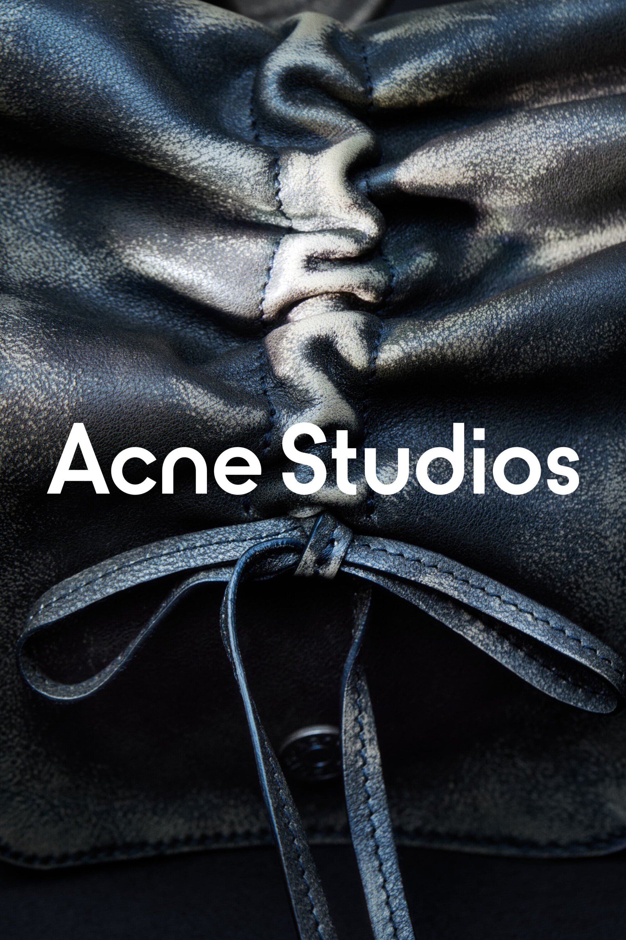 Close-up of a black leather bag with ruched detailing and tied straps, featuring the Acne Studios logo in white text.