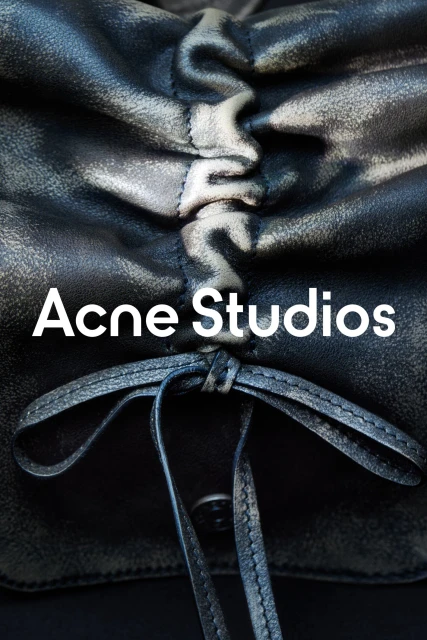 Close-up of a black leather bag with ruched detailing and tied straps, featuring the Acne Studios logo in white text.