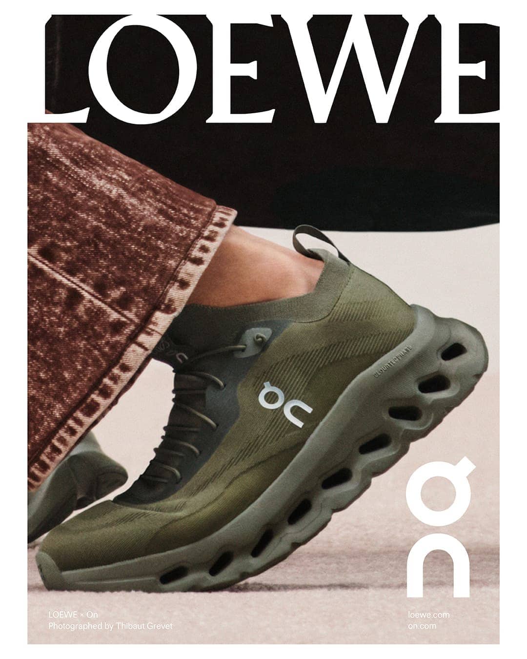 Olive-green Loewe x On Cloudtilt 2.0 sneaker on a light carpet with a model’s leg and white Loewe logo in the background.