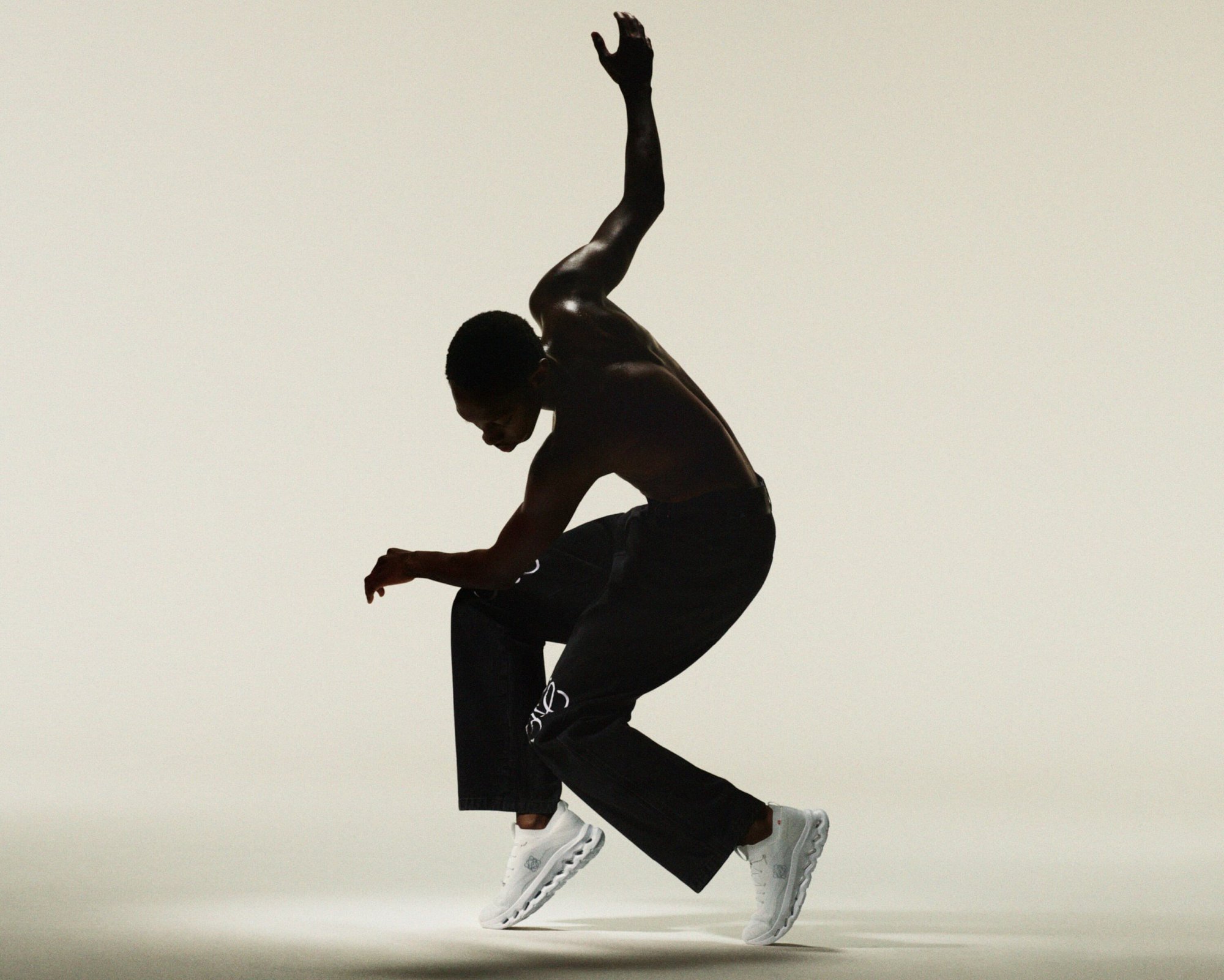 Athletic Black man in motion wearing black pants and white running shoes in a dynamic pose against a light background.