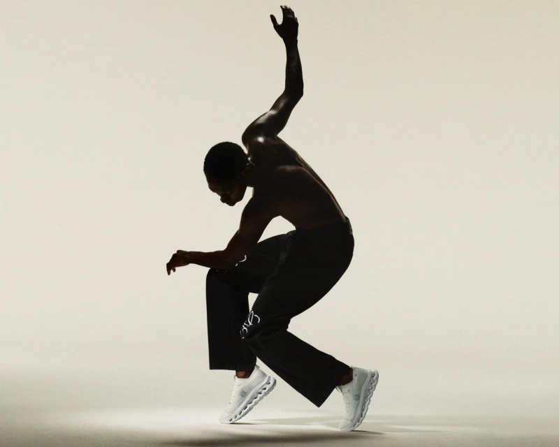 Athletic Black man in motion wearing black pants and white running shoes in a dynamic pose against a light background.