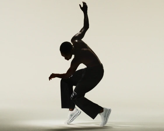 Athletic Black man in motion wearing black pants and white running shoes in a dynamic pose against a light background.