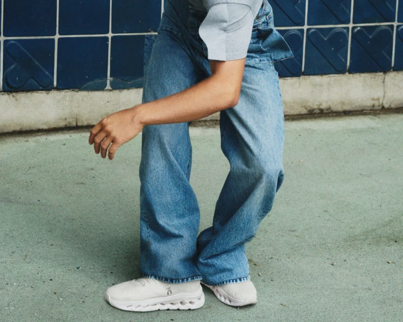 Person in denim outfit and white sneakers stands against a blue tiled wall with a light green floor, captured in a fashion-forward shot.