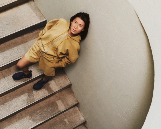 Person in yellow hooded sweatshirt and matching shorts standing on stairs, wearing dark sneakers, captured from a high-angle perspective.