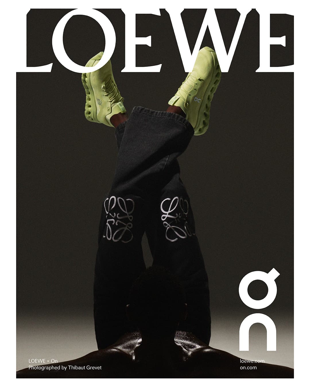 Fashion editorial featuring an upside down view of a person wearing Loewe jeans and light green On running shoes against a grey background.