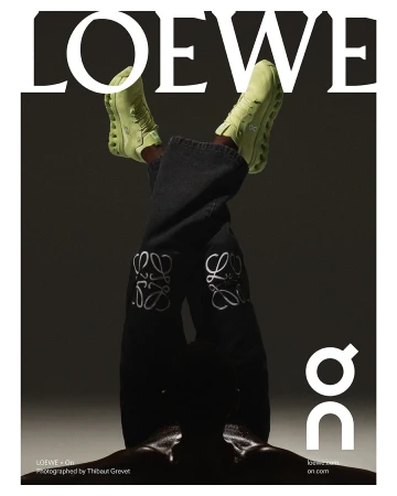 Fashion editorial featuring an upside down view of a person wearing Loewe jeans and light green On running shoes against a grey background.