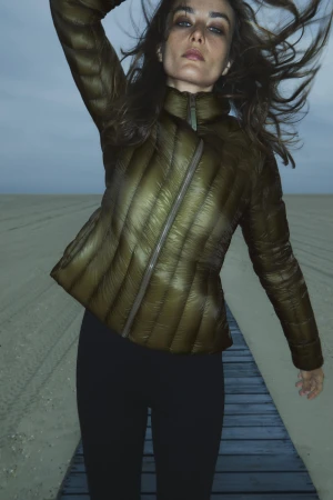 A woman in a quilted jacket poses on a beach boardwalk under an evening sky, showcasing fashion and outdoor lifestyle photography.