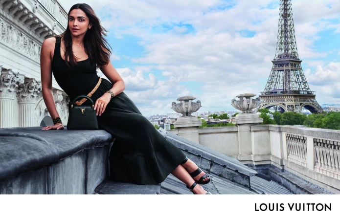 Fashion shot of a brunette woman in a black dress posing on a Paris rooftop with the Eiffel Tower in the background on a sunny day.