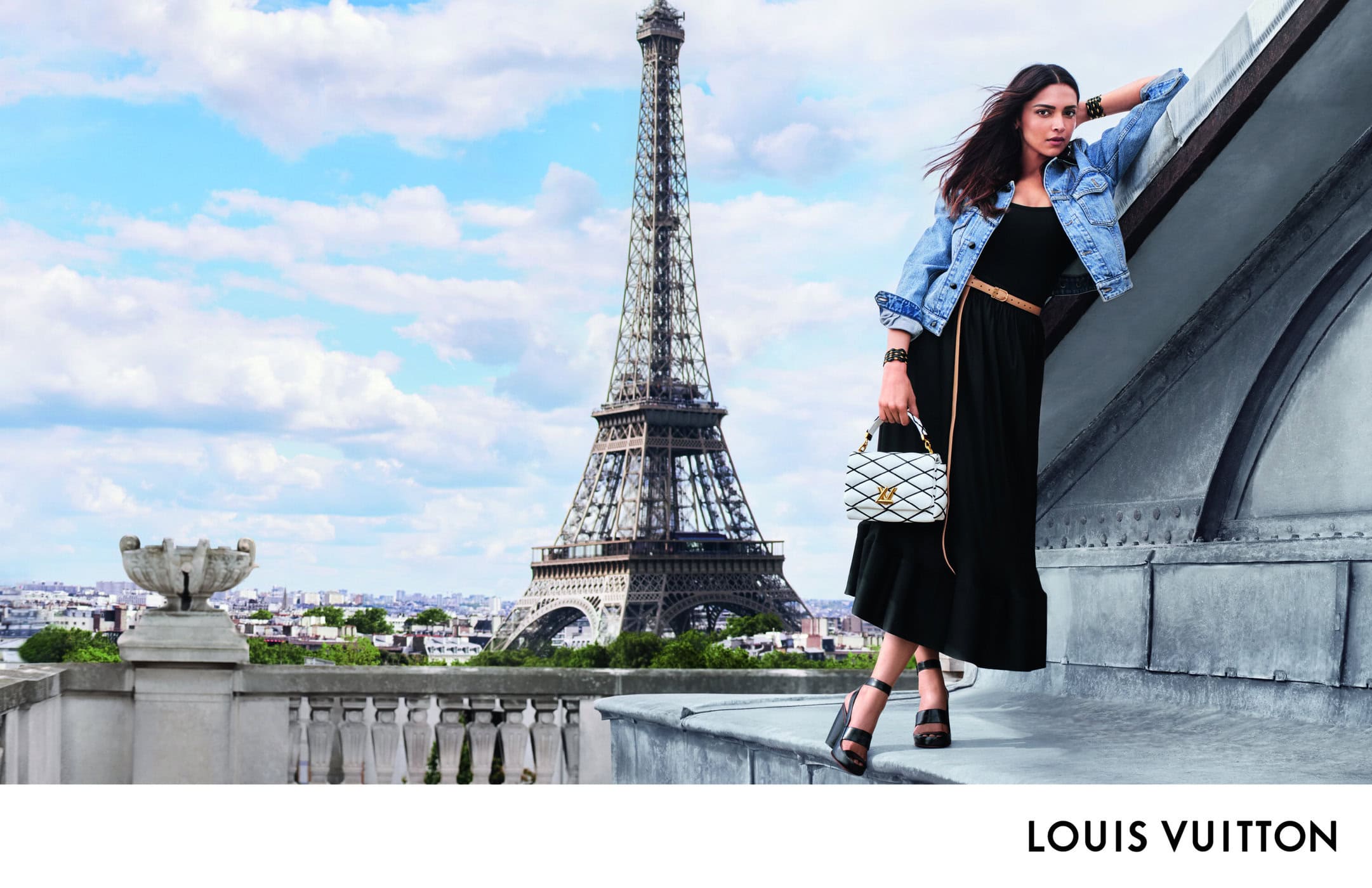 Model Deepika Padukone in denim jacket and black dress leaning on rooftop with Eiffel Tower background for Louis Vuitton