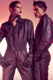 Two models in matching dark jumpsuits posing against a warm gradient background for Ferrari Fall 2023 campaign.