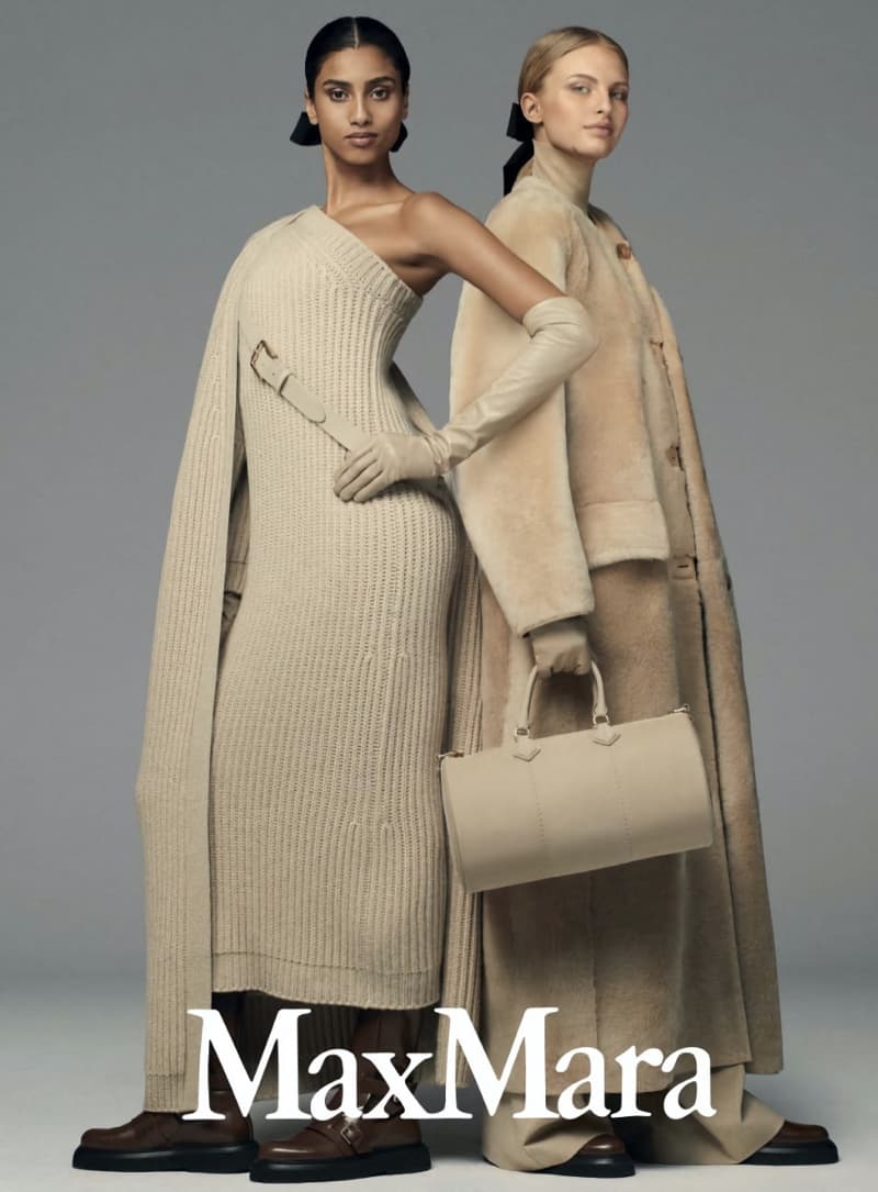 Two female models in a studio setting showcasing Max Mara apparel. One wears a beige knit dress and the other a long coat and leather bag.