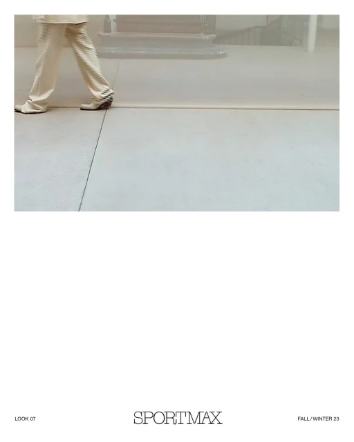 Fashion shot of a person walking with tan trousers and shoes on a grey surface in a diffused bright indoor setting, for Sportmax.