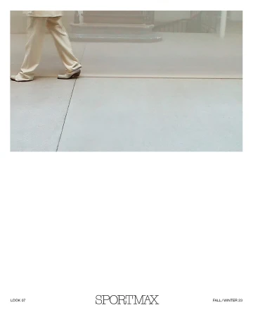 Fashion shot of a person walking with tan trousers and shoes on a grey surface in a diffused bright indoor setting, for Sportmax.
