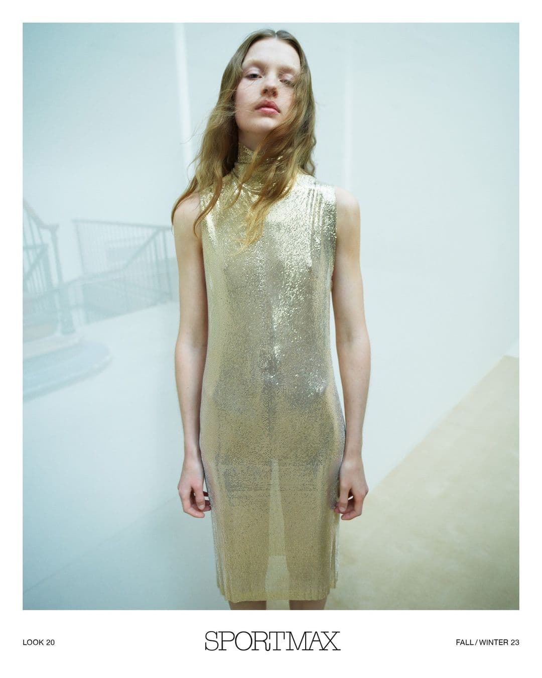 A fair-skinned woman with wavy light brown hair poses indoors wearing a sparkling gold sleeveless midi dress and neutral makeup.
