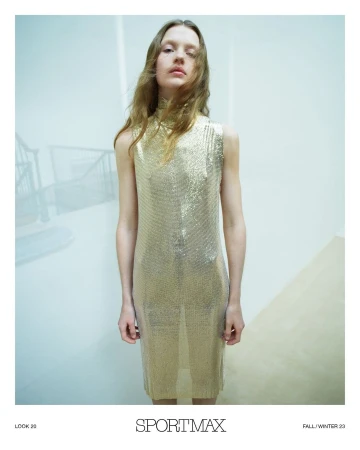 A fair-skinned woman with wavy light brown hair poses indoors wearing a sparkling gold sleeveless midi dress and neutral makeup.