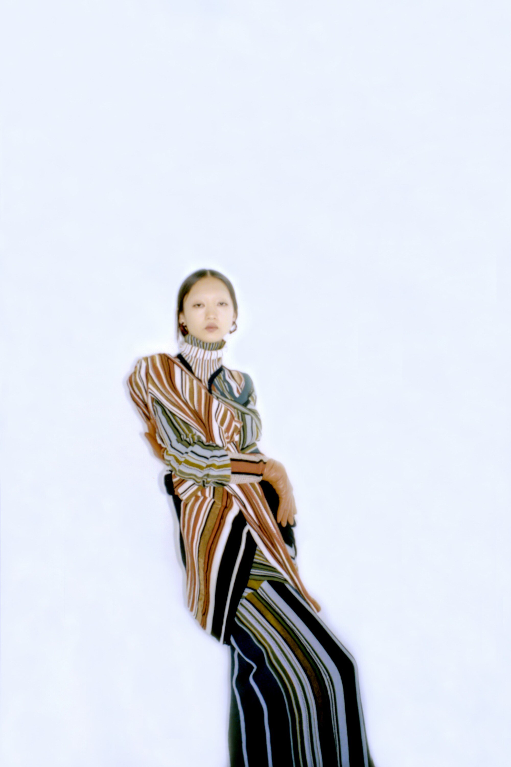 Young woman posing in striped dress against a white backdrop in a fashion style full shot with high angle and shallow depth of field.