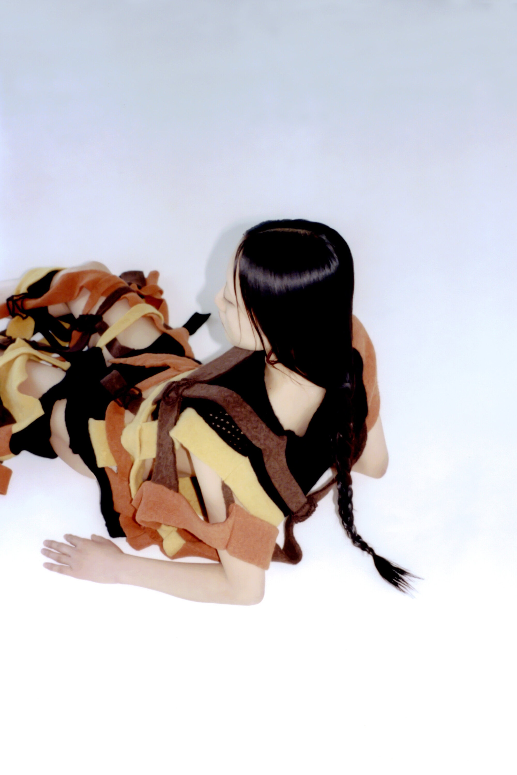 Overhead shot of a young female model with long braided hair, wearing a striped garment, posing against a white backdrop in a photo studio.