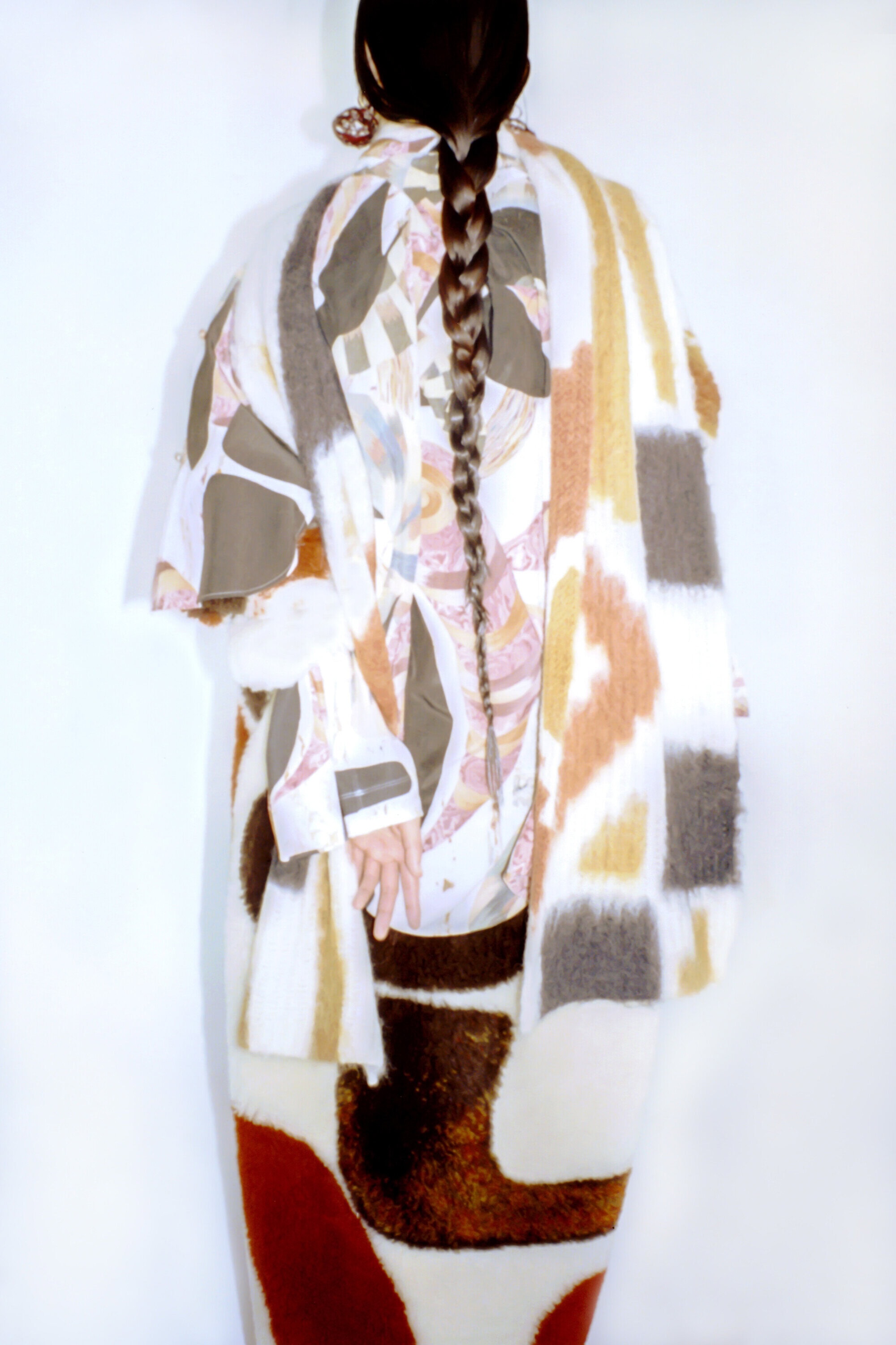 Back view of a woman with a braid wearing a unique, colorful patterned outfit in a bright, neutral indoor studio setting.