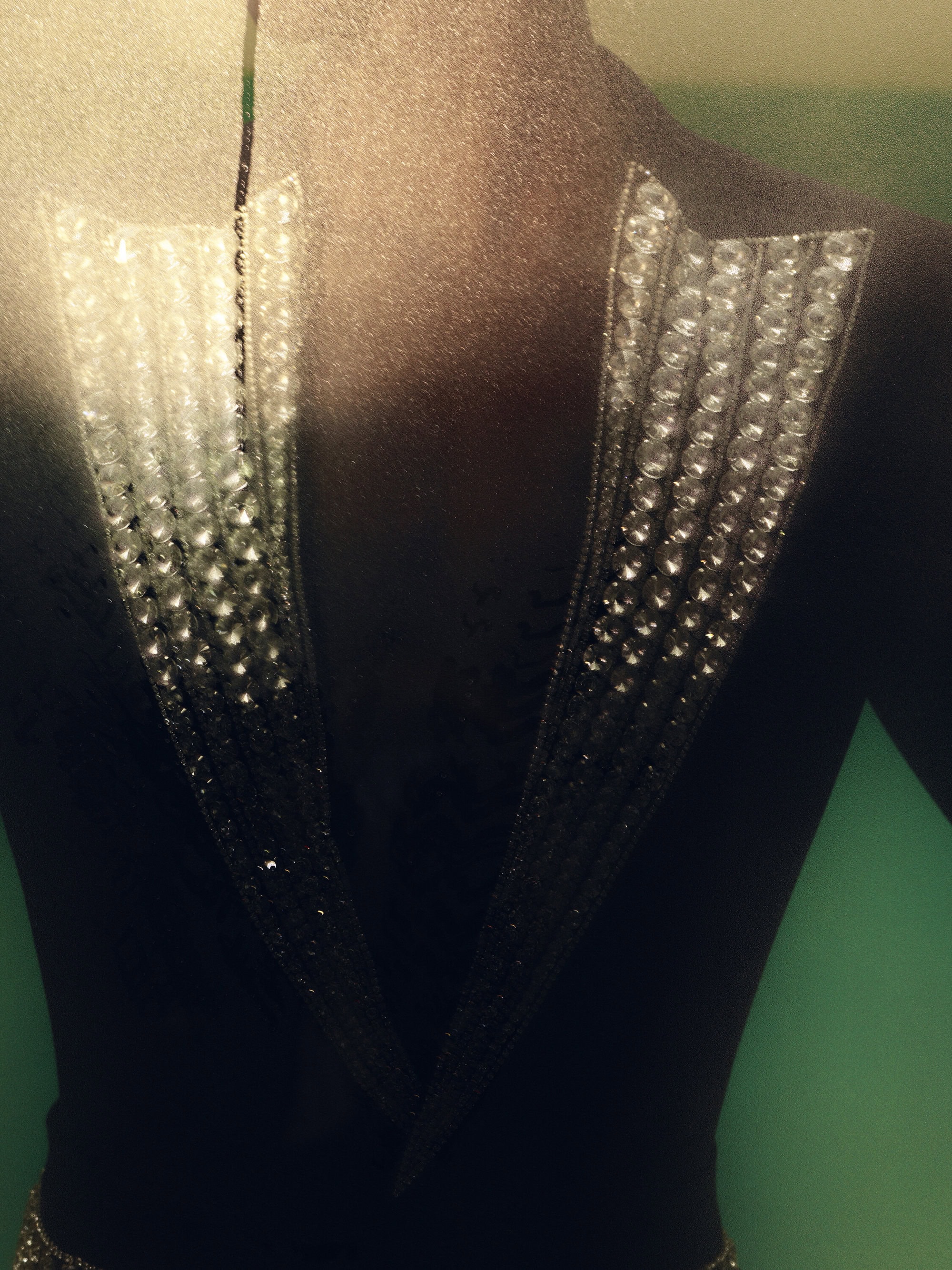 Close-up of a person wearing a black top with silver crystal embellishments, against a muted green background in a studio setting.