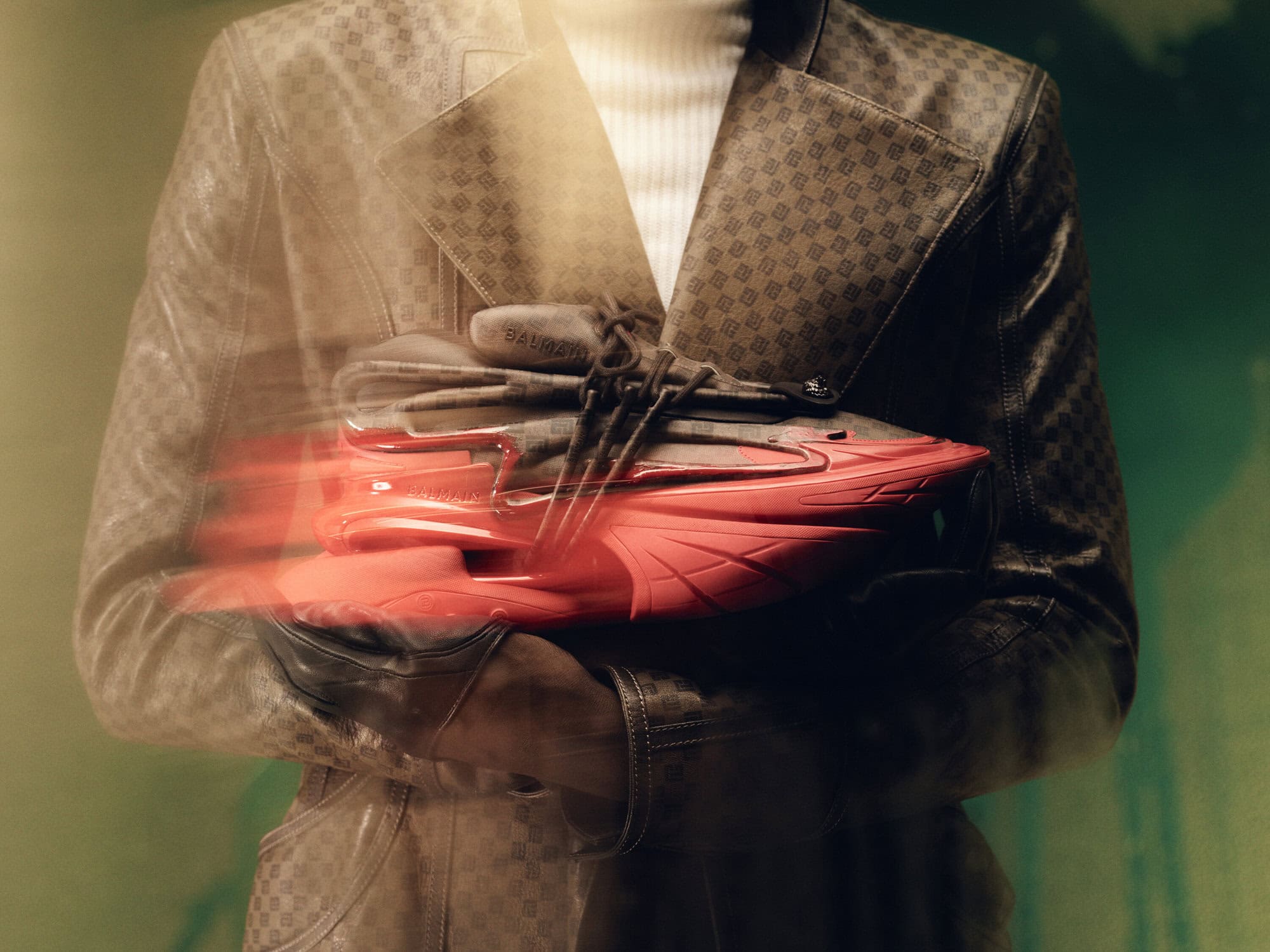 Close-up of Balmain sneakers being held by a model wearing a patterned jacket, capturing a blend of fashion and footwear.