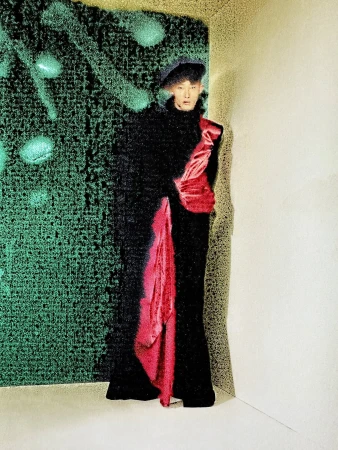 A person stands in a black outfit with a red sash against a green textured wall in an indoor studio setting with soft lighting.