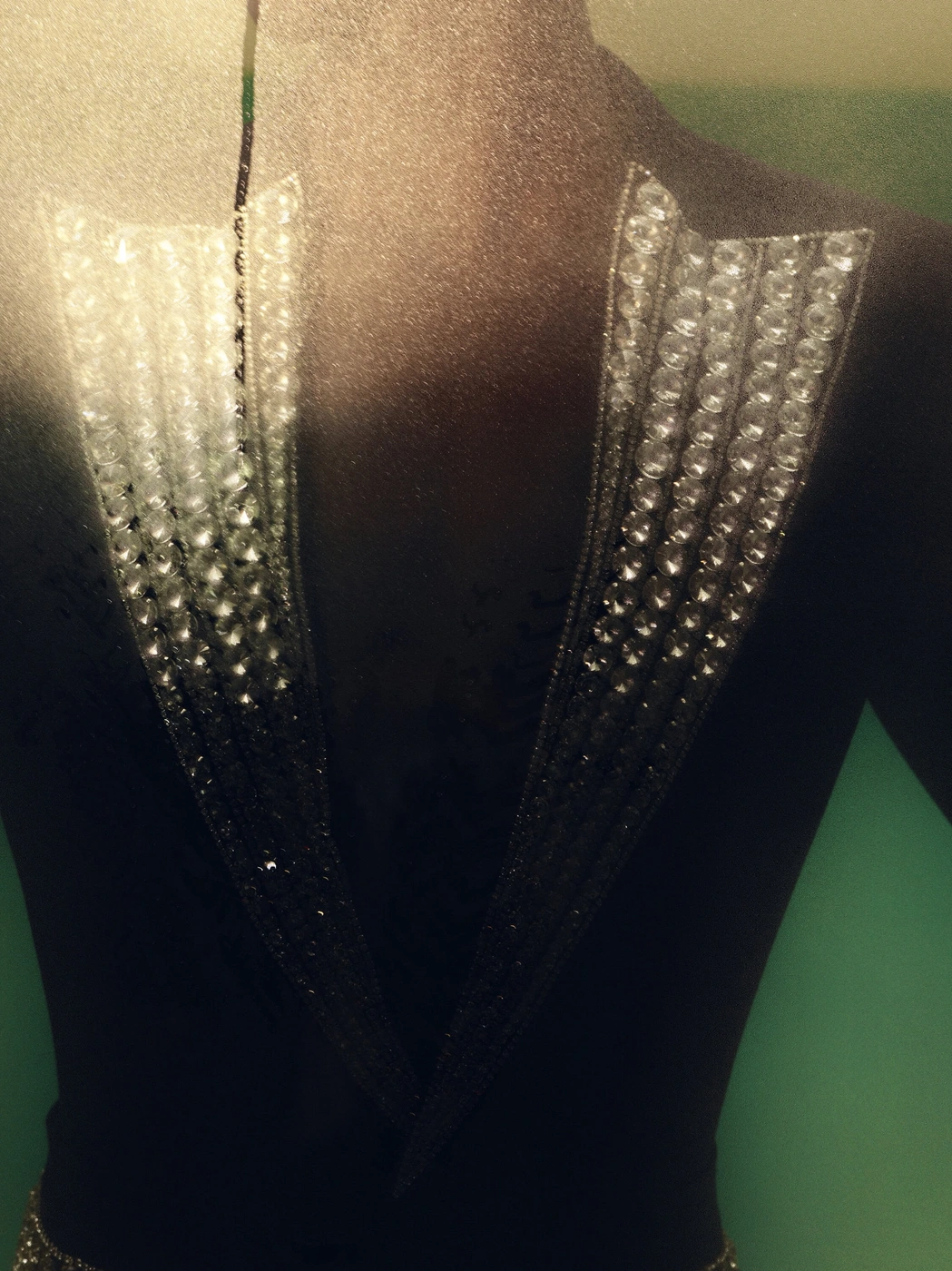 Close-up of crystal and rhinestone embellishments on a black tailored garment displayed on a dress form.