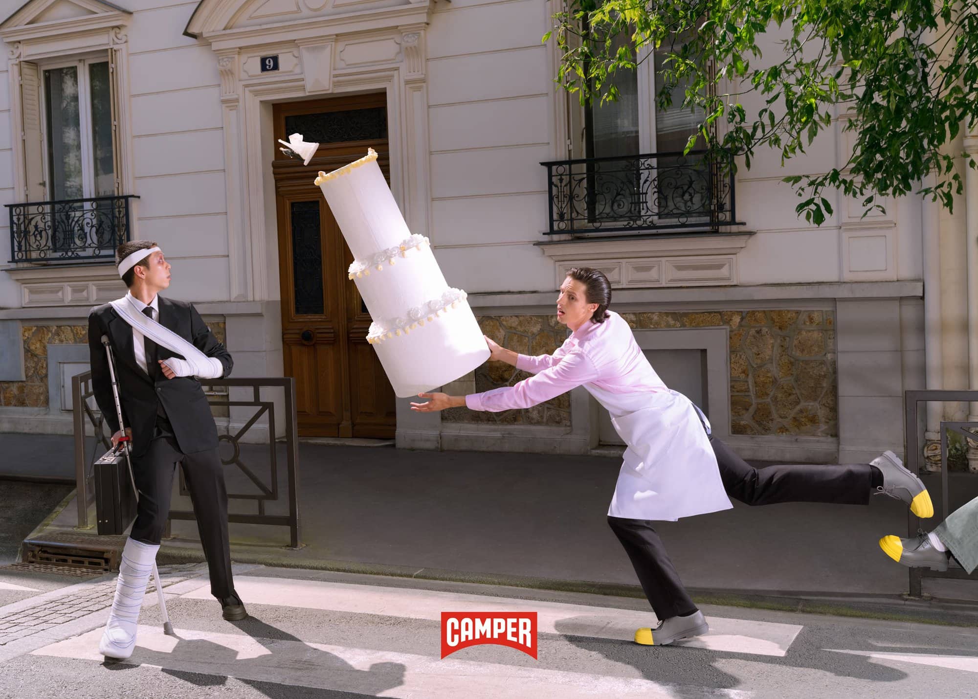 Humorous fashion ad with two people on a street, one injured with a cane and the other appearing to drop a large wedding cake.