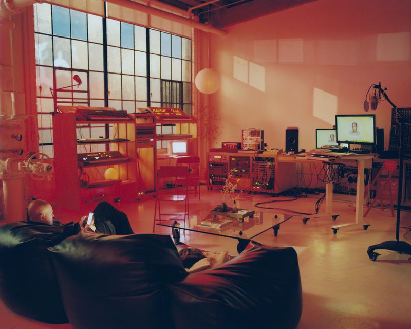 An adult is reclining on a beanbag chair in a music studio with various audio equipment, computers, and large windows.