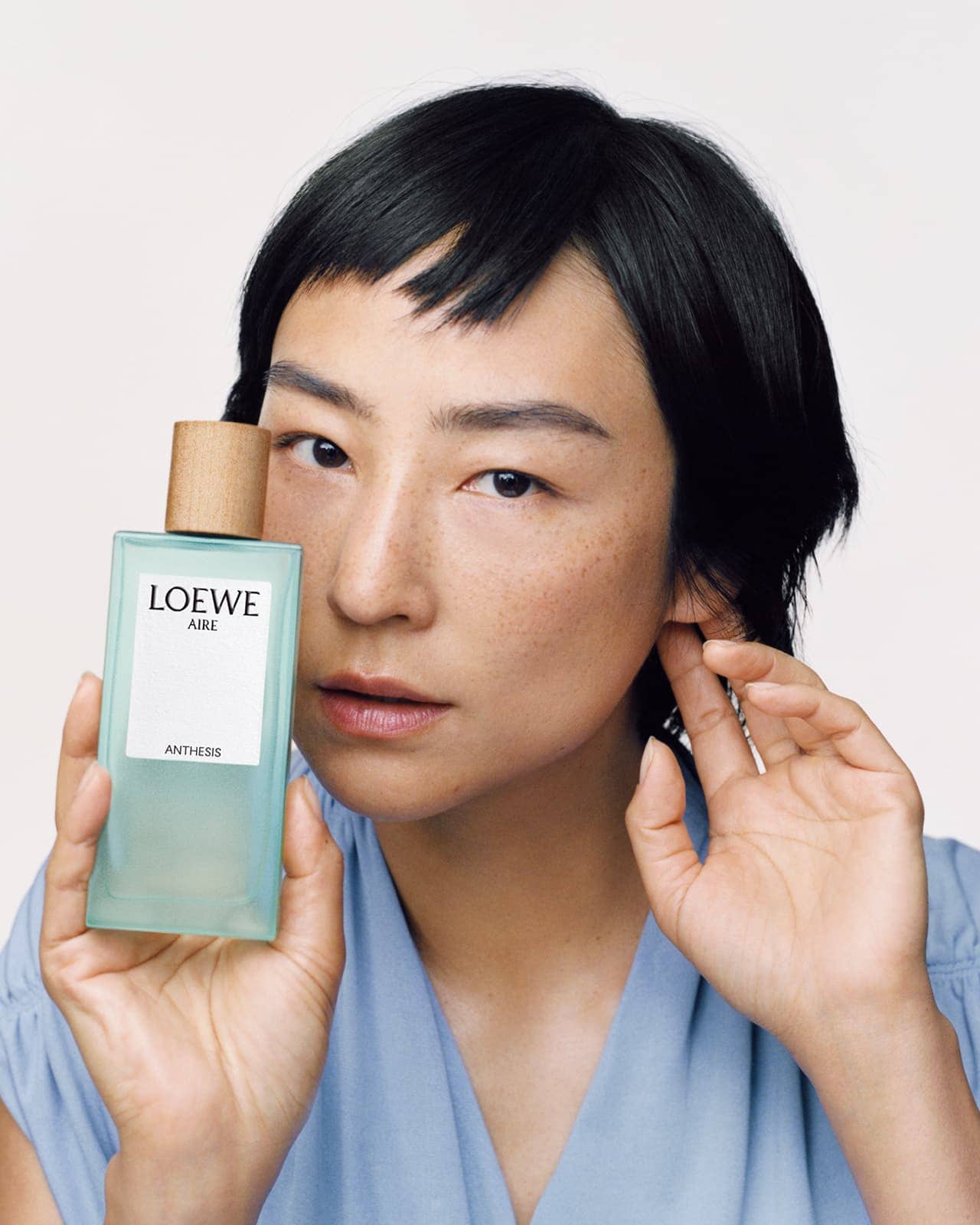 Asian woman with black hair poses with Loewe Aire Anthesis perfume. Focus on beauty, fashion, and product shot in a photo studio.