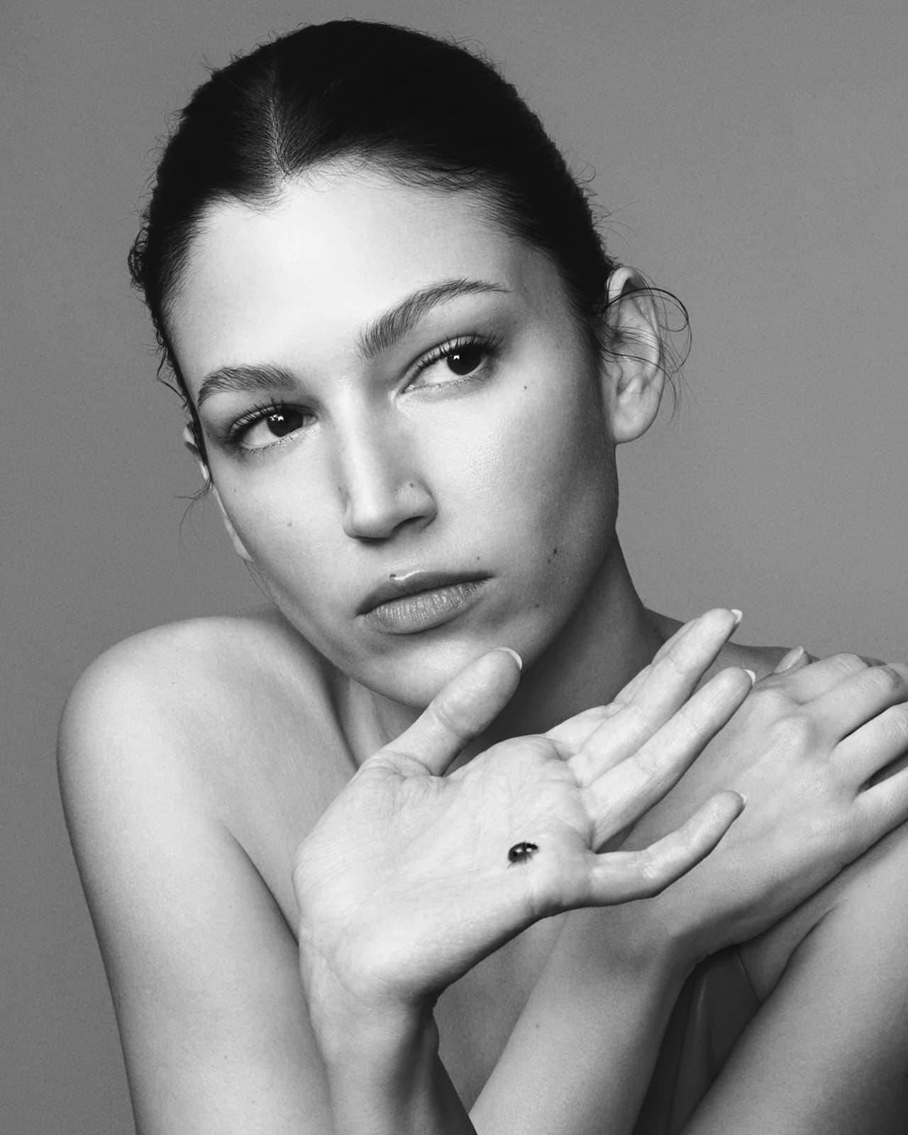 Close-up portrait of a light-skinned woman with dark hair in a bun, holding a small, round object on her open palm, studio shot.