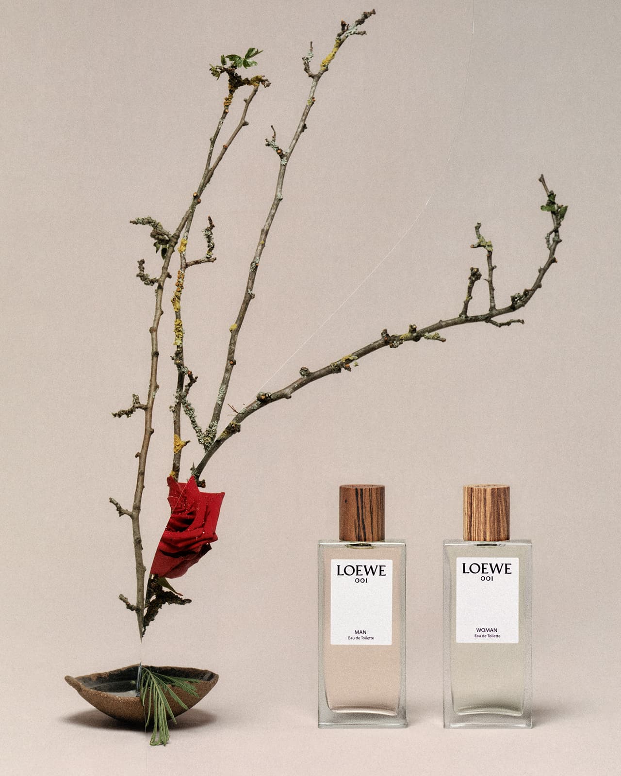 Still life shot featuring Loewe 001 perfumes, arranged with dry branches and a bowl, set against a neutral-toned backdrop. 