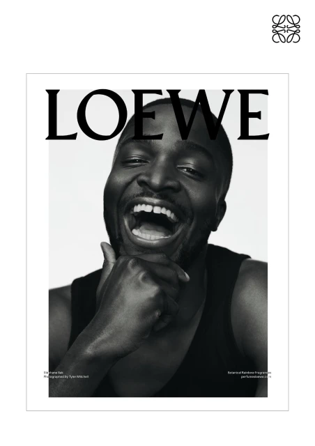 Black and white fashion magazine cover featuring an African American man with his hand to his chin laughing and wearing a tank top.