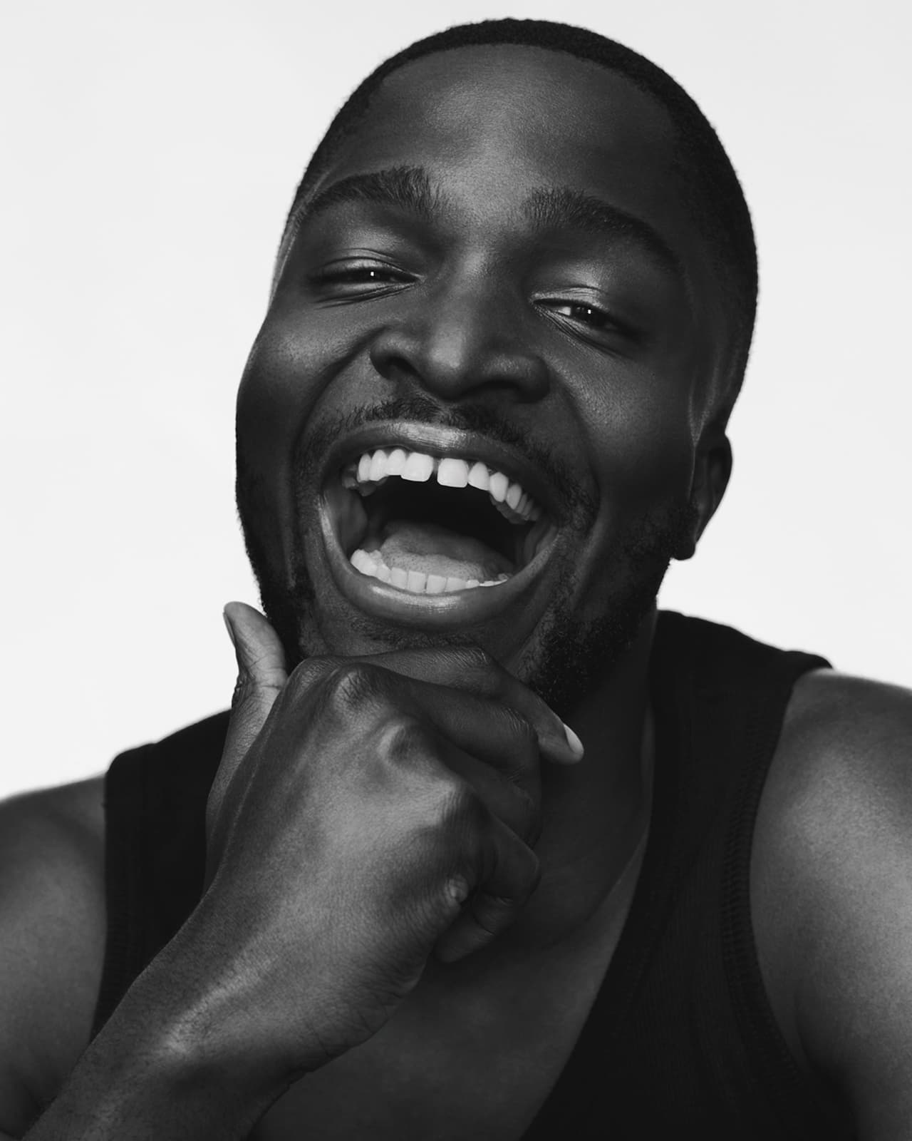 Black and white portrait of a happy African American man laughing with his hand on his chin against a white background.