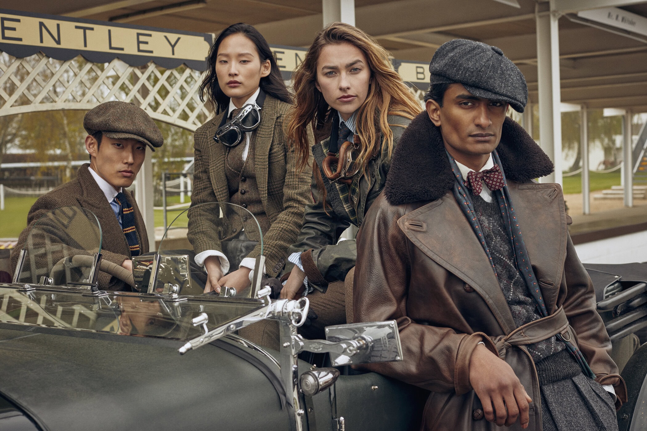 Four people in vintage clothing posing with a classic green Bentley car, creating a stylish and nostalgic scene.