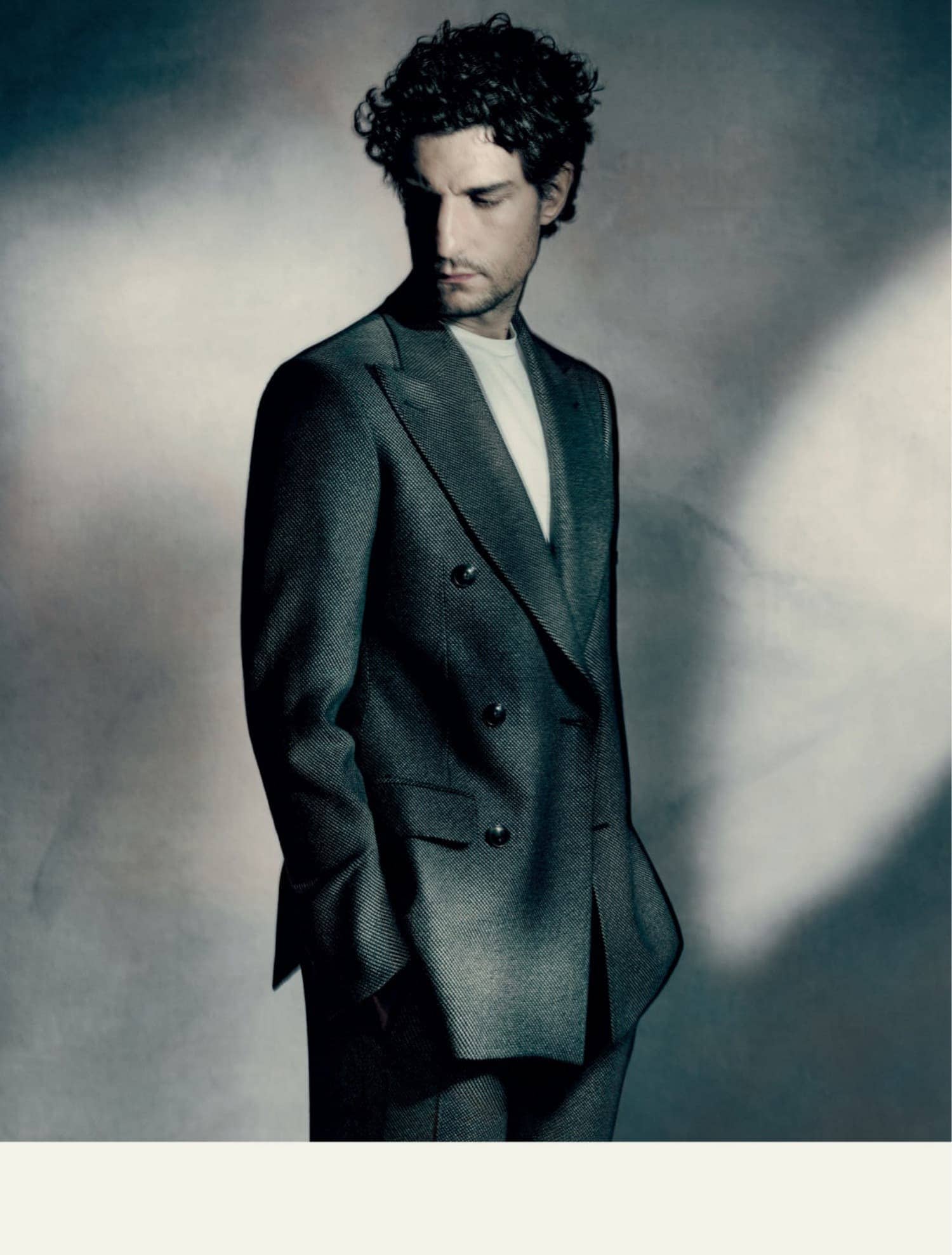 Portrait of a handsome man wearing a suit jacket, looking down against a softly lit grey background. Studio lighting.