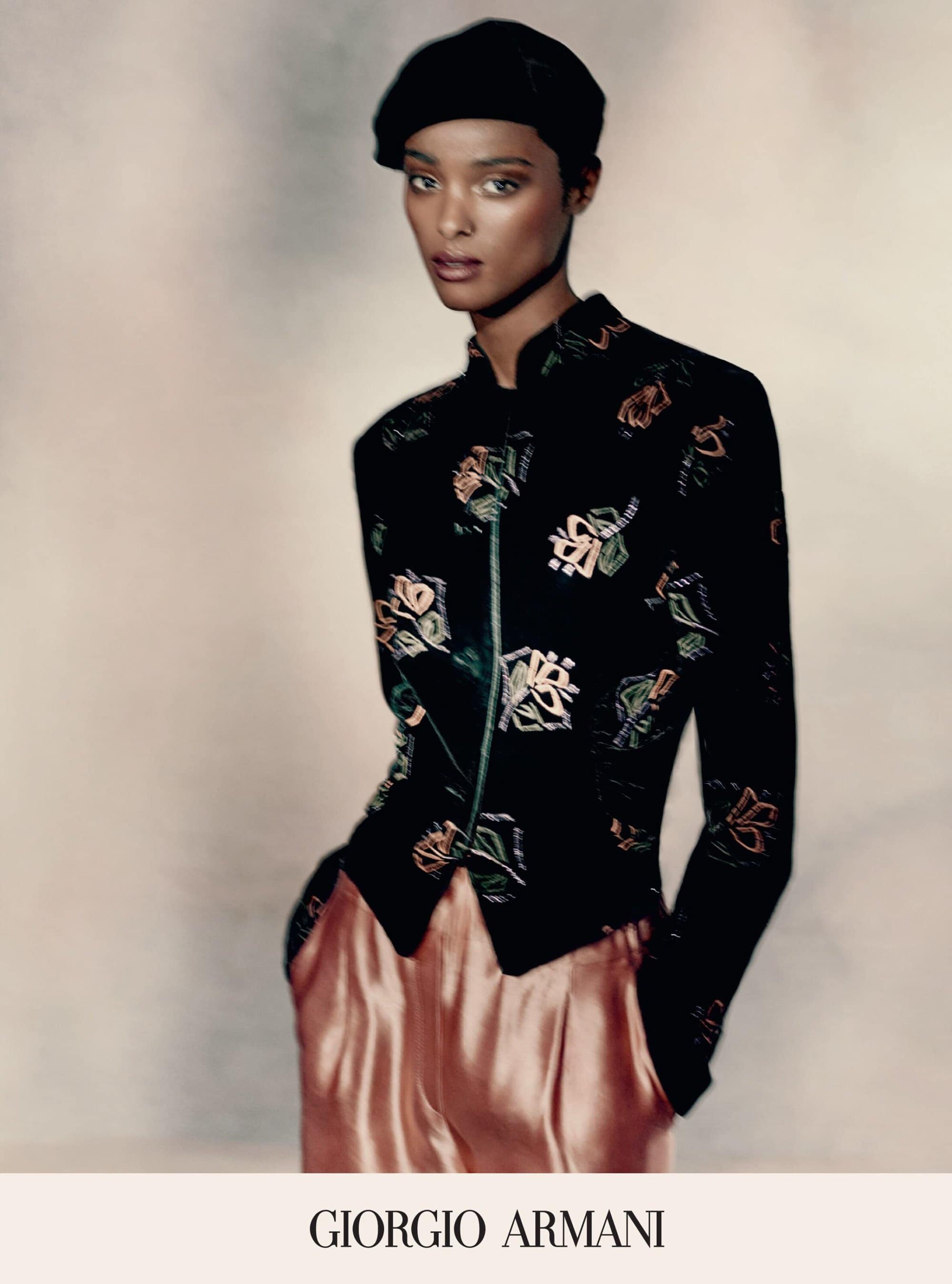Fashion image of an adult female posing in a black patterned jacket and pink pants, wearing a black beret against a neutral backdrop.