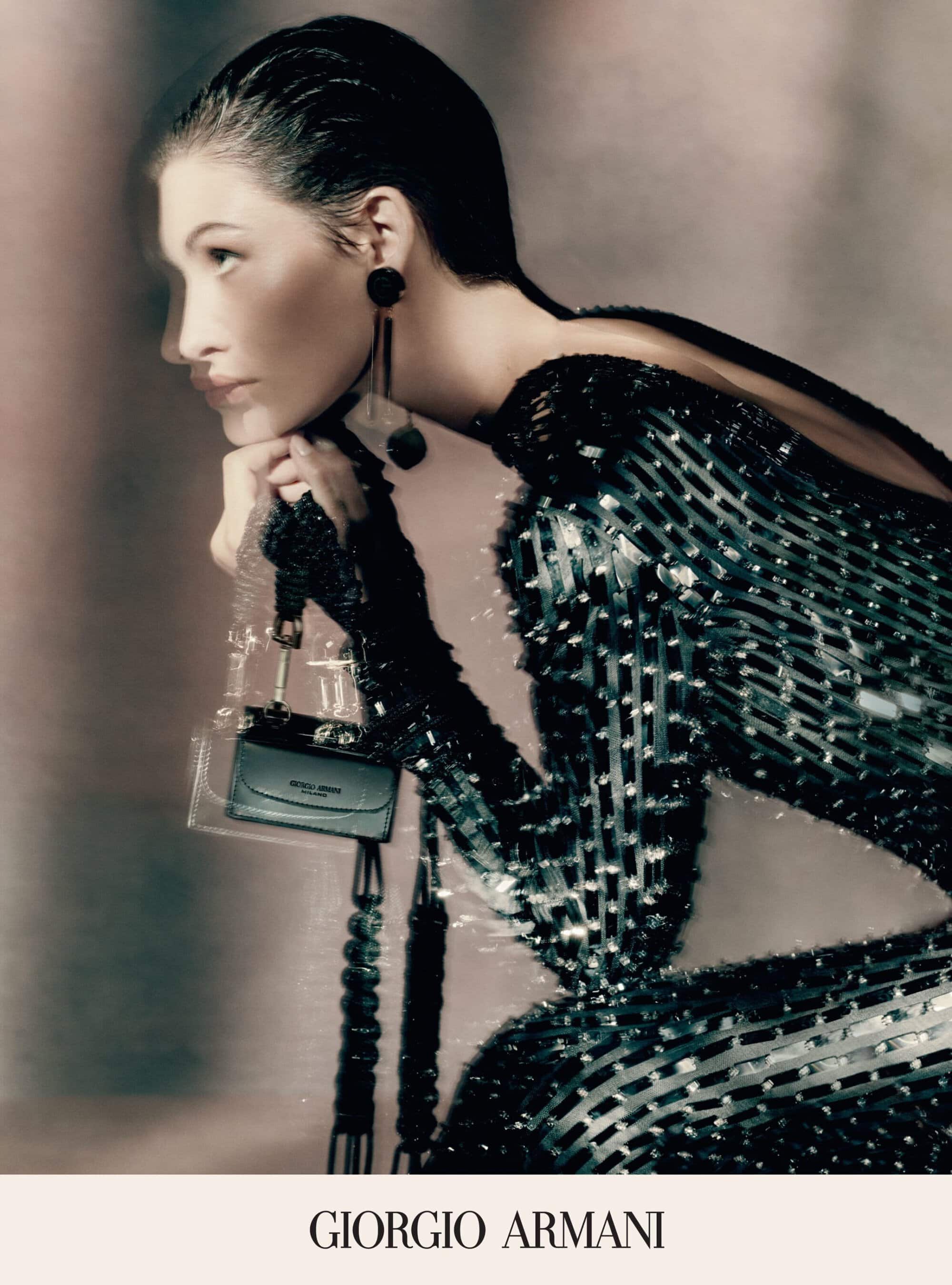 Fashion portrait of woman in black sequin dress and large earrings, resting head on hand, holding a small dark purse.