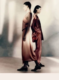Two models standing back-to-back in matching satin garments against a neutral mottled studio backdrop