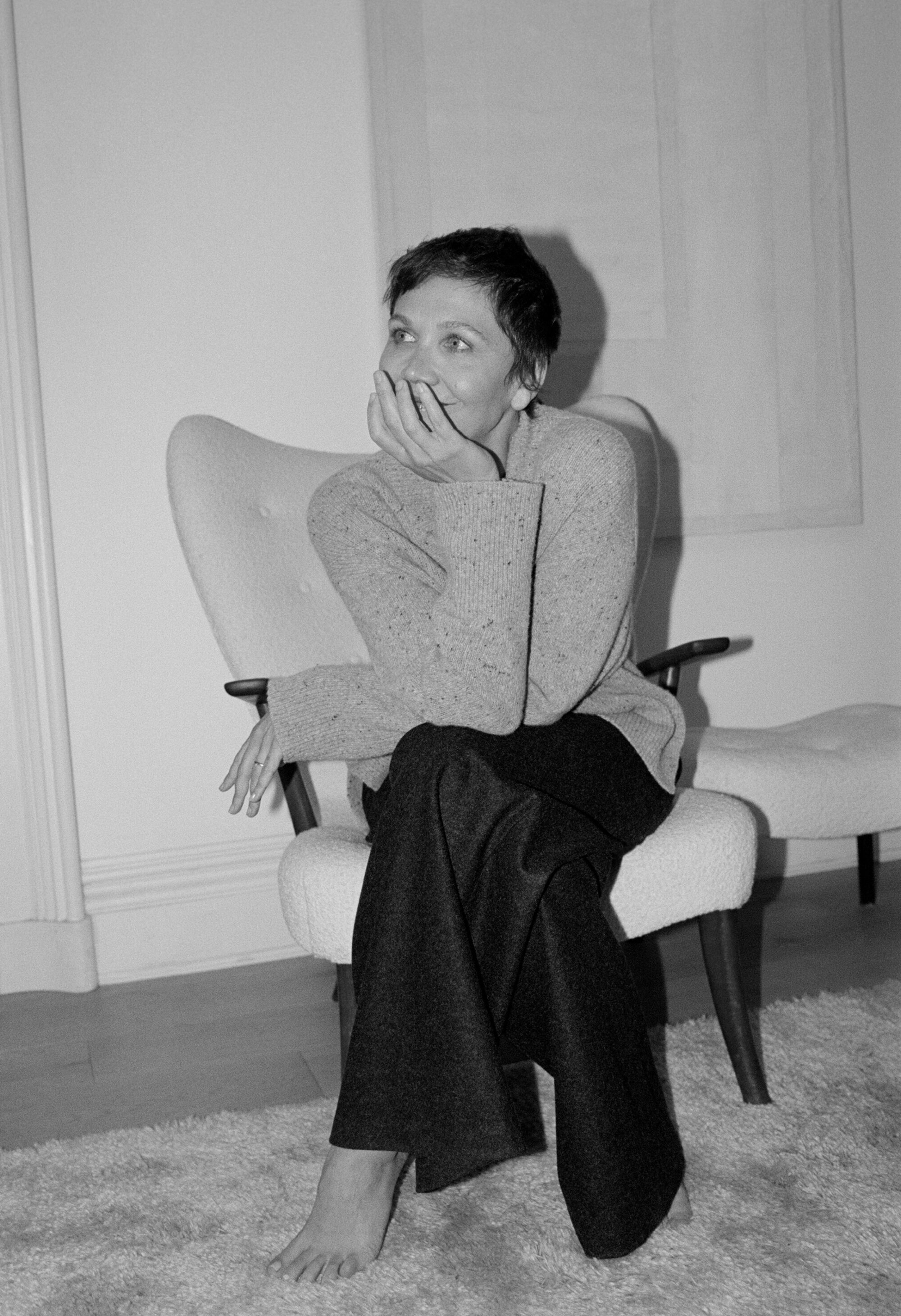 Woman sitting in mid-century chair in a black and white photograph in an interior space with an arm to her face looking aside.