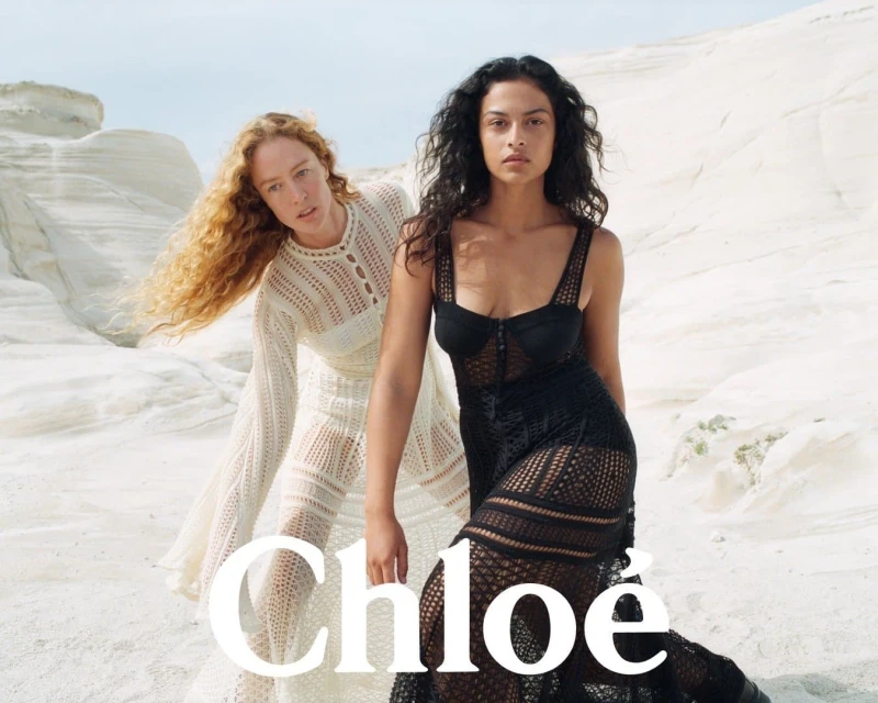 Two women in elegant dresses pose against a light-colored rocky landscape, showcasing fashion apparel and outdoor styling.