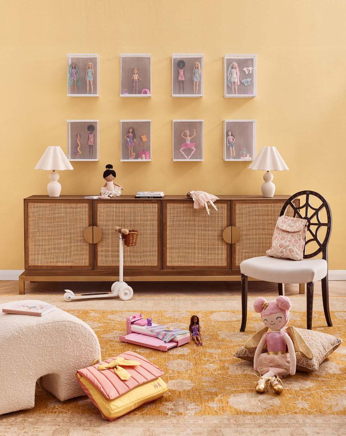Doll collection display: Dolls in cases mounted on a wall above a wooden console with doll accessories and toys in a kids' playroom.